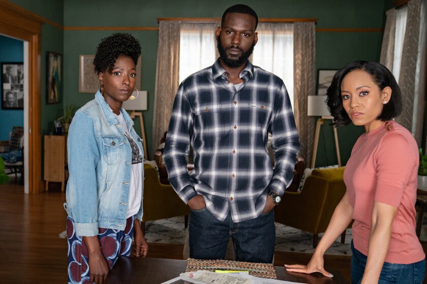 A man and two women stand at a table in a living area.