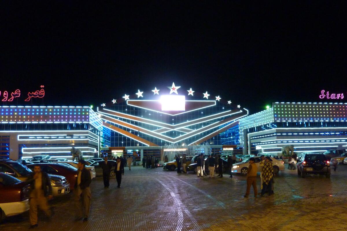 Afghan men walk past the entrance of a brilliantly illuminated wedding hall in Kabul.