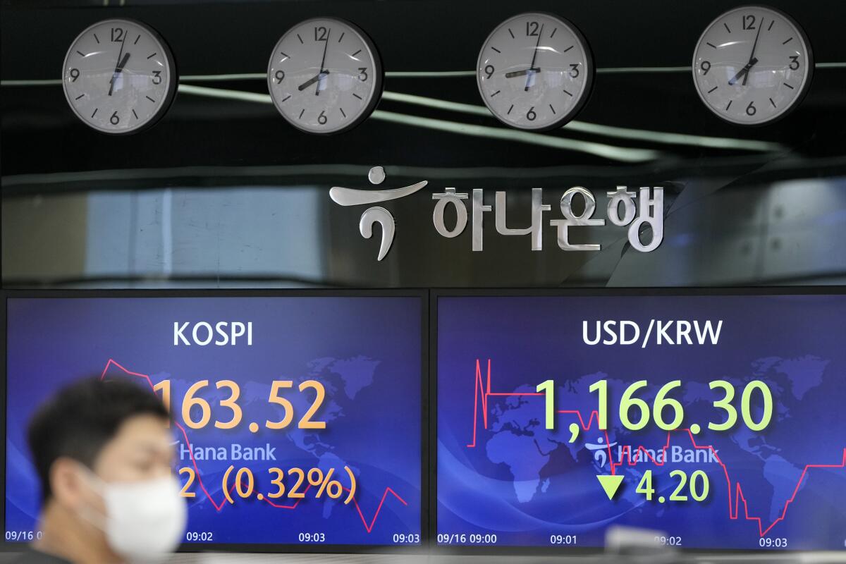 A currency trader walks by screens showing the Korea Composite Stock Price Index (KOSPI), left, and the foreign exchange rate between U.S. dollar and South Korean won at a foreign exchange dealing room in Seoul, South Korea, Thursday, Sept. 16, 2021. Stocks were mostly lower in Asia on Thursday after Japan and China released data that were weaker than expected. (AP Photo/Lee Jin-man)