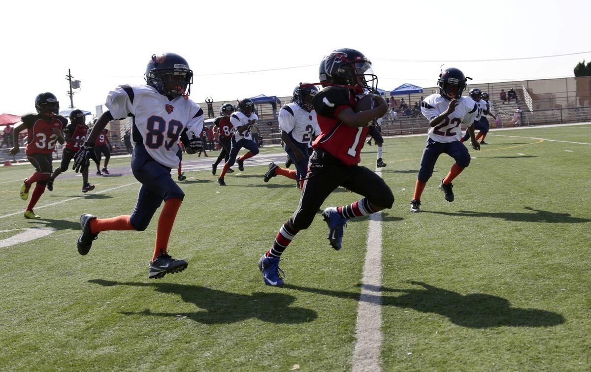 The LAPD-coached youth football team Watts Bears (in white) pursue a member of the Southern California Falcons during a 2013 game. The players are 7 to 9 years old.