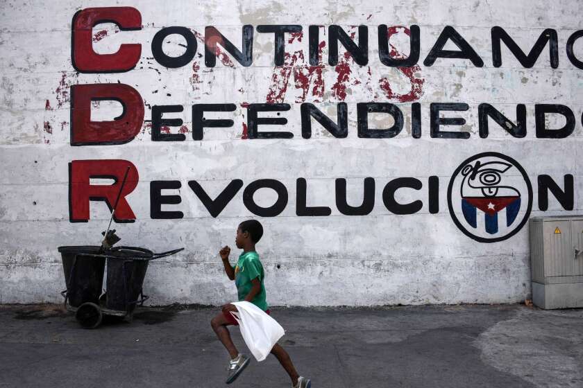 In Havana on the eve of President Obama's visit, a child runs in front of a wall reading "We keep defending the revolution."