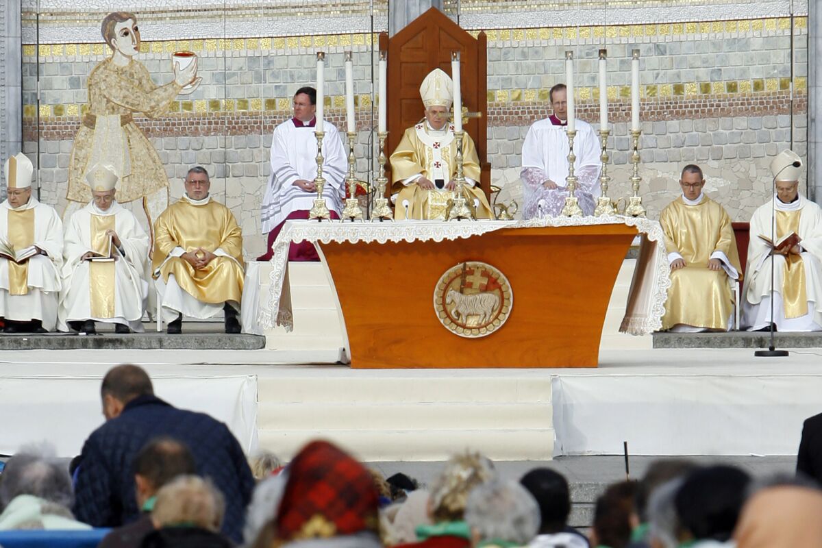 FILE - Pope Benedict XVI, center, celebrates a Mass in front of the Basilica of the Rosary in Lourdes, southwestern France, on Sept. 15, 2008. Behind him is one of the mosaics by Rev. Marko Ivan Rupnik, who was declared excommunicated in 2020 for committing one of the worst crimes in church law – using the confessional to absolve a woman with whom he had engaged in sexual activity. Officials at the Catholic shrine in Lourdes, France announced the creation of a study group Friday, March 31, 2023, to decide what to do with the sanctuary’s mosaics, its most famous but now controversial attraction. (AP Photo/Alessandra Tarantino)