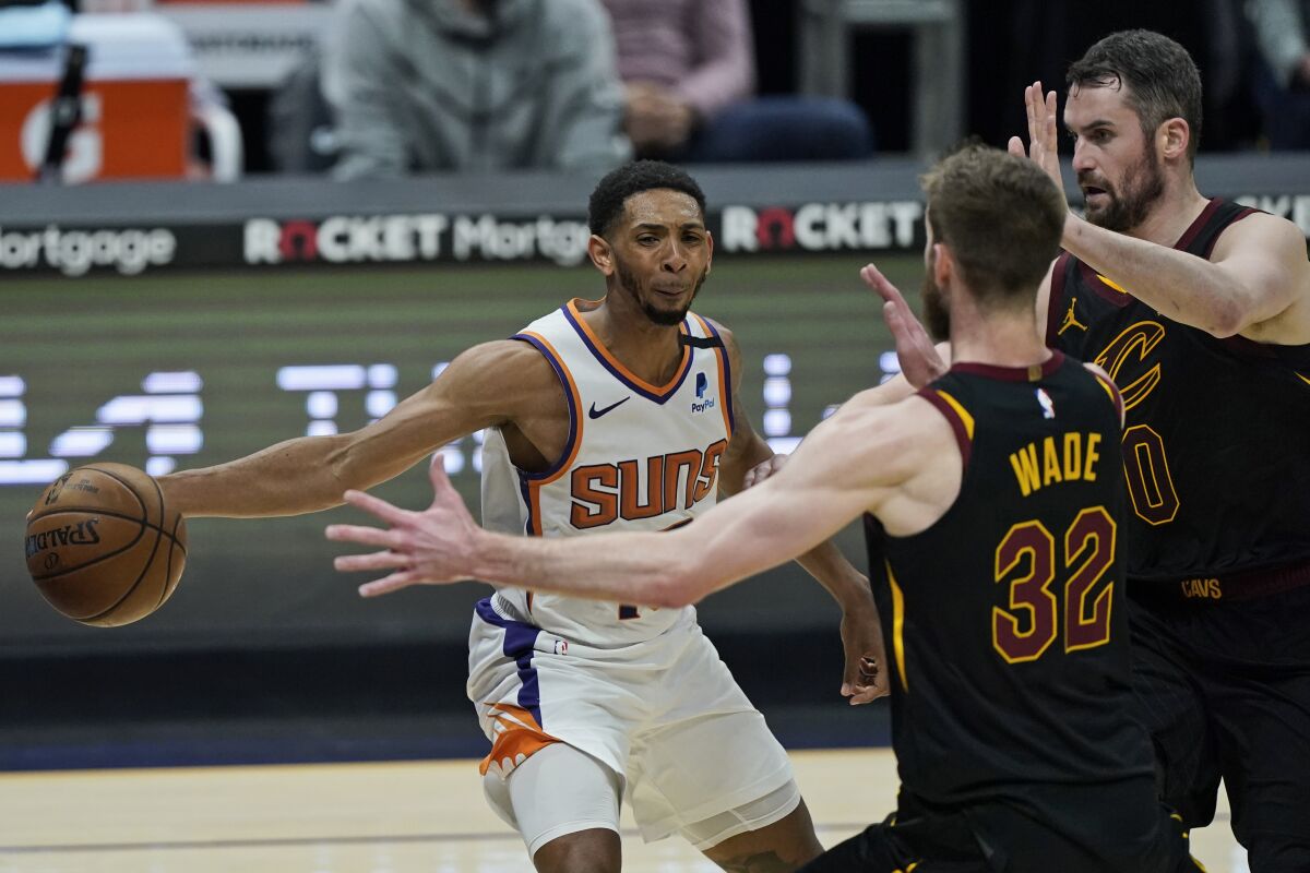 Phoenix Suns' Cameron Payne, left, passes around Cleveland Cavaliers' Dean Wade and Kevin Love in the first half of an NBA basketball game, Tuesday, May 4, 2021, in Cleveland. (AP Photo/Tony Dejak)