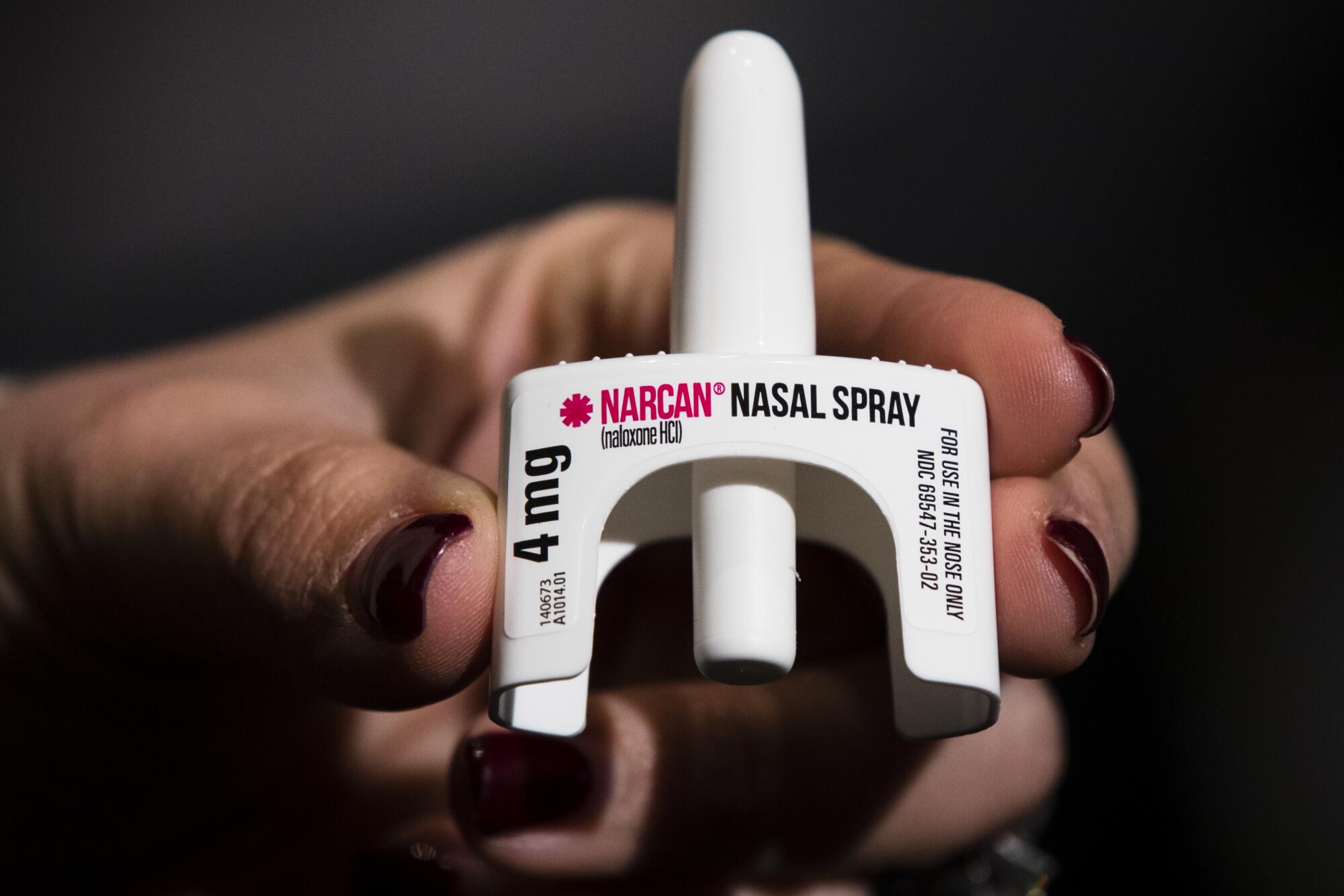 A close view of a hand with dark-red painted fingernails holding Narcan nasal spray