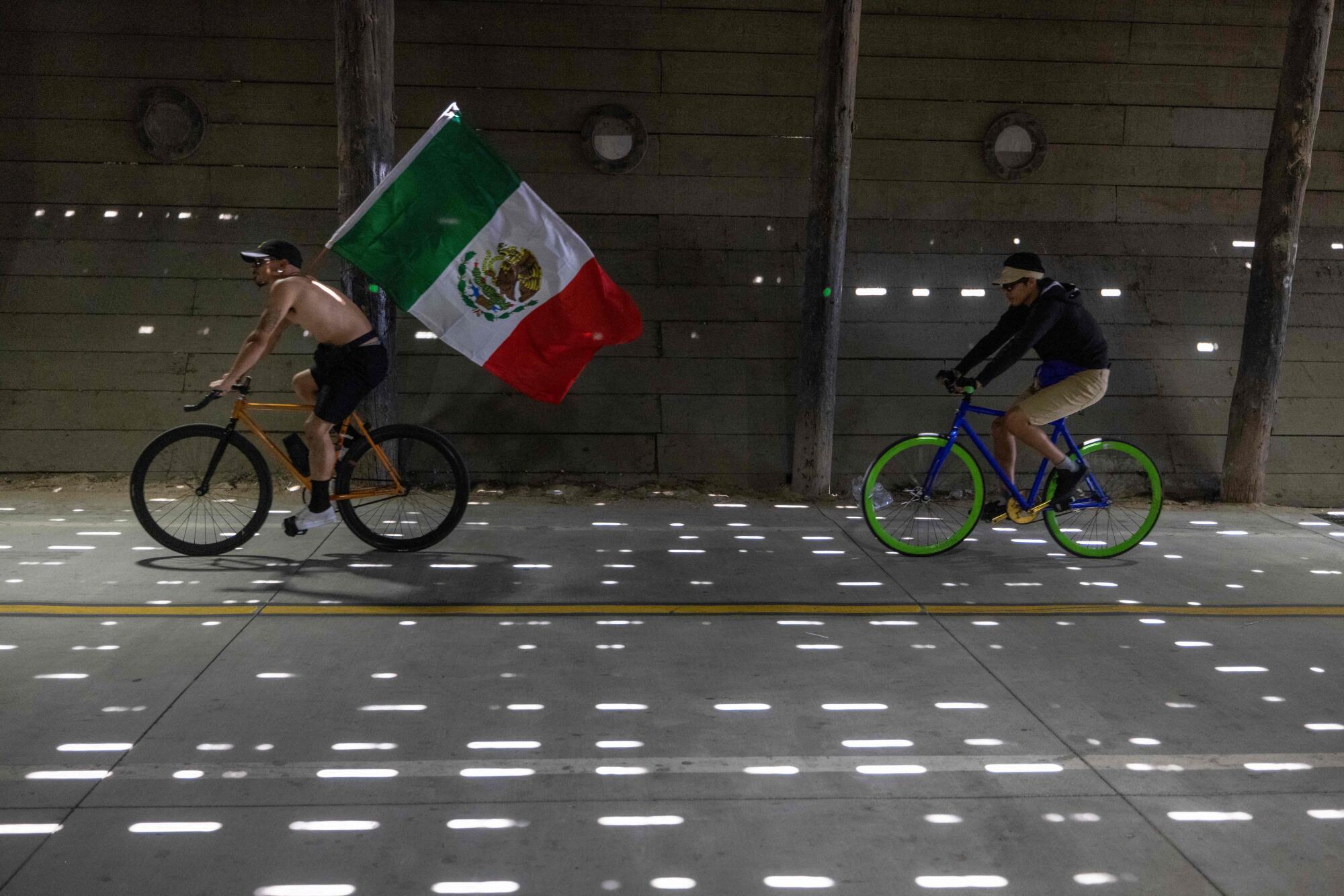 A man flies the flag of Mexico from a bike passing under the Santa Monica Pier.