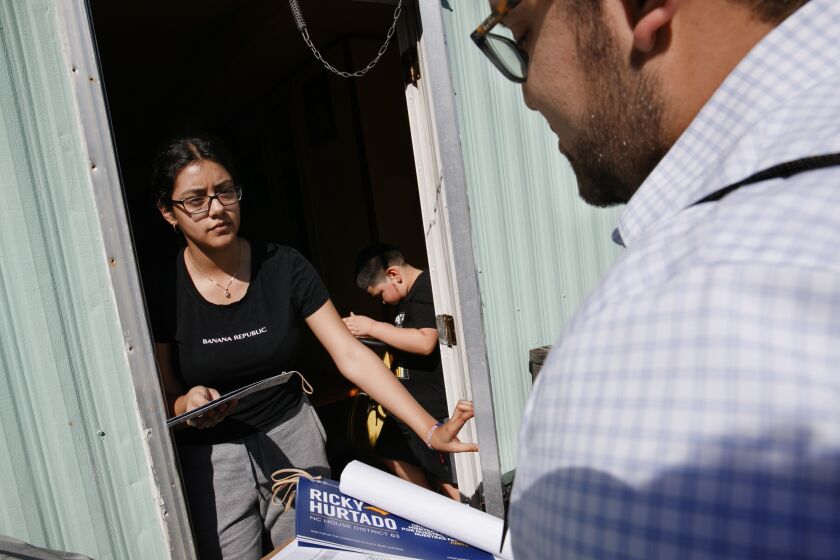 Evelyn Lara, 19, with her brother Iker, 7, opens the door as Ricky Hurtado, a Democratic candidate for the North Carolina state house, canvasses voters in a largely Latino trailer community, in Burlington, N.C., Sunday, March 8, 2020. (AP Photo/Jacquelyn Martin)