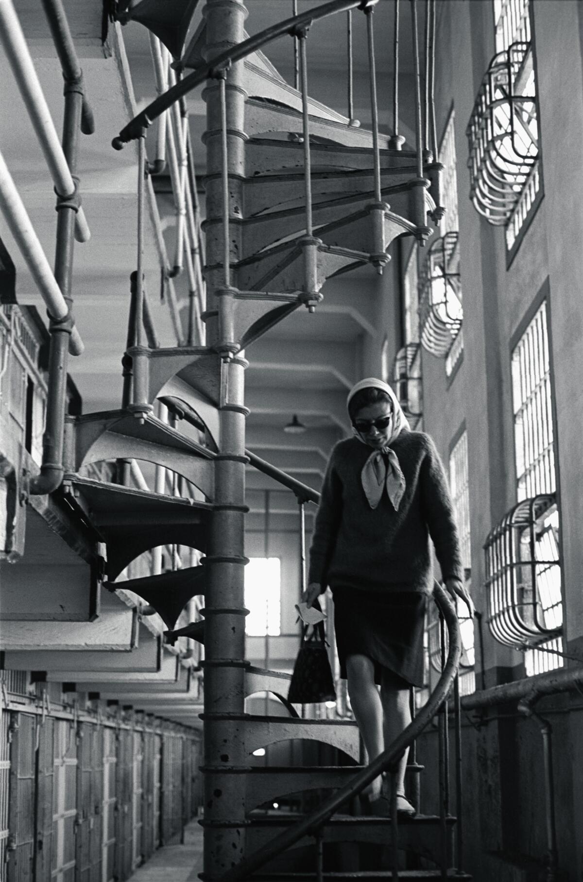 A black-and-white photo of a woman in a headscarf walking down a spiral staircase 