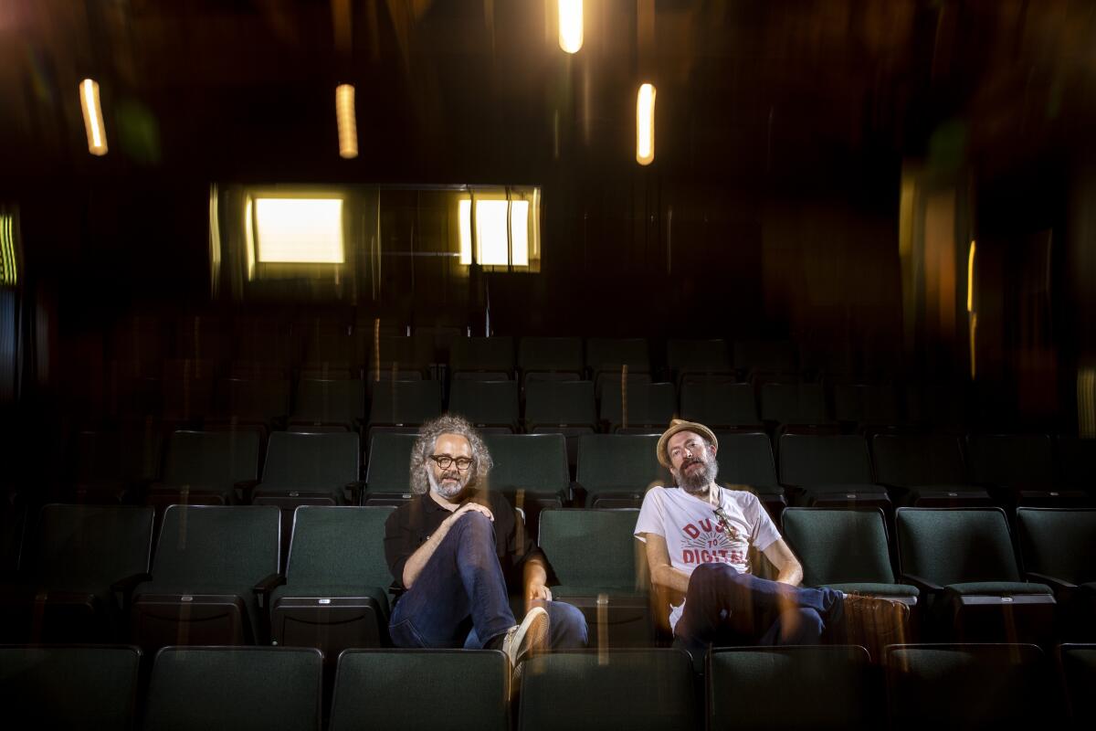 Two men sitting in green upholstered theater seats