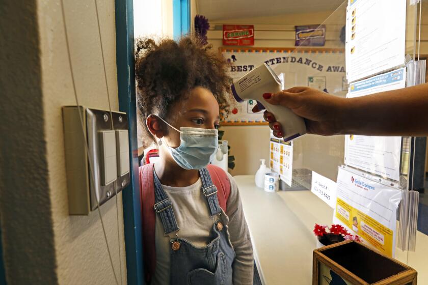 Los Angeles, California-June 23, 2021-Zadie Williams, age 8, gets her temperature checked before entering summer school in the fourth grade at Hooper Avenue School in Central Los Angeles on June 23, 2021. All students must wear a mask at all times. Summer school has started in all grades in Los Angeles Unified Schools. (Carolyn Cole / Los Angeles Times)