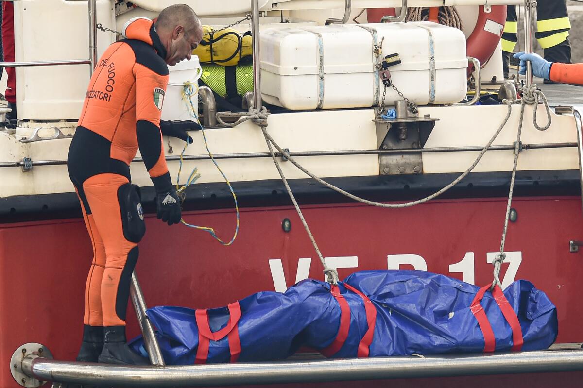 Italian firefighter divers bring ashore in a plastic bag the body of a shipwreck victim.