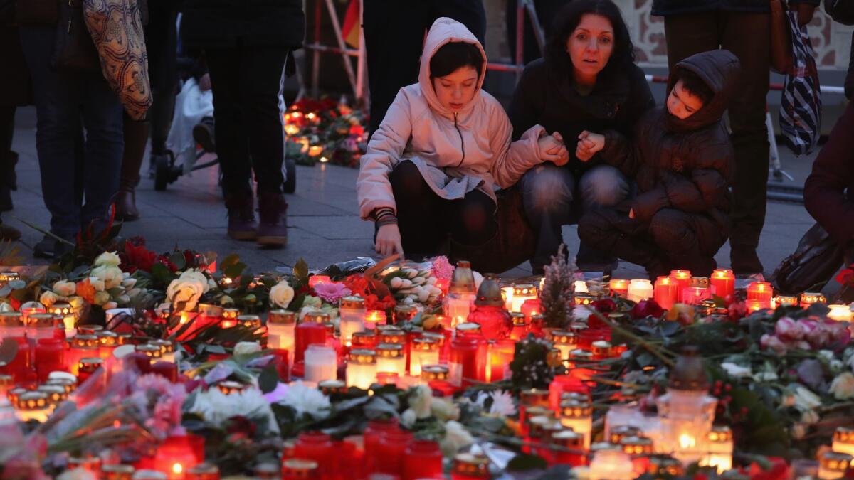Christine Tan and her children Ralia, 5, and Mathilde, 12, look at flowers and candles left at a makeshift memorial on Dec. 21, 2016, near the site where a truck was driven into a Christmas market in Berlin.