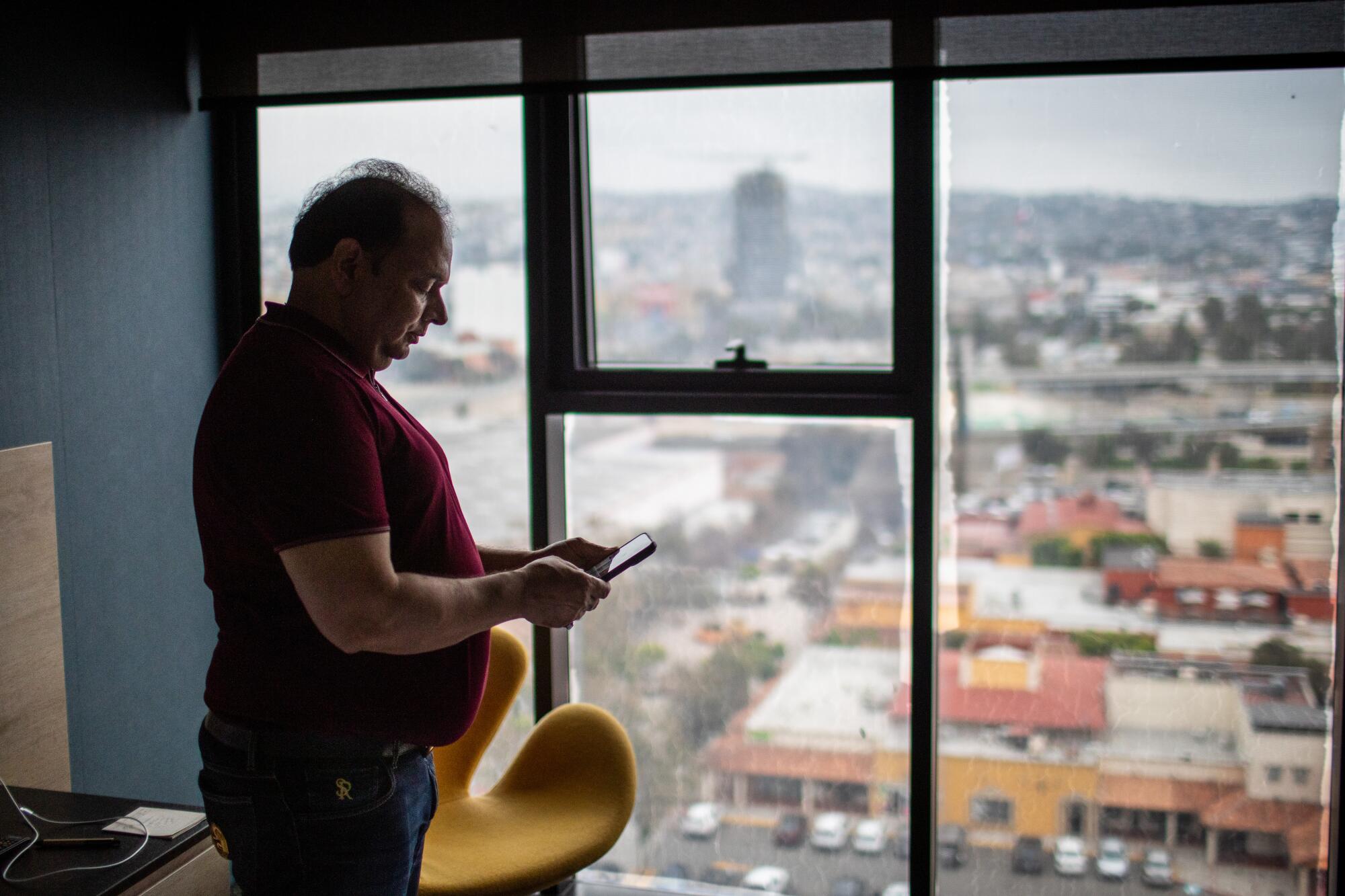 Dr. Pradyuman Singh checks his phone while standing next to a window in a room overlooking a cityscape.