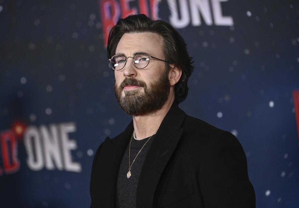 A bearded Chris Evans wearing glasses and a black T-shirt and blazer poses at a premiere