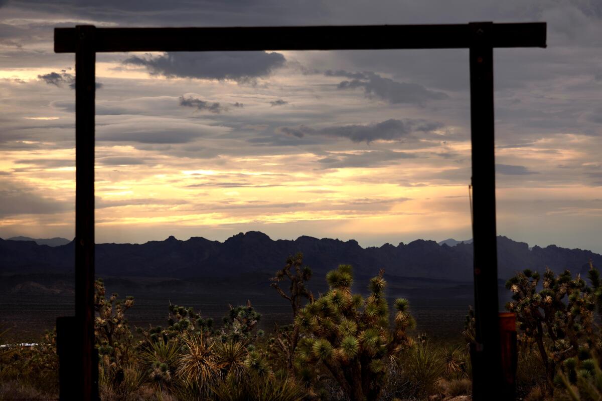 A gate is silhouetted at sunset, with mountains and clouds in the distance.