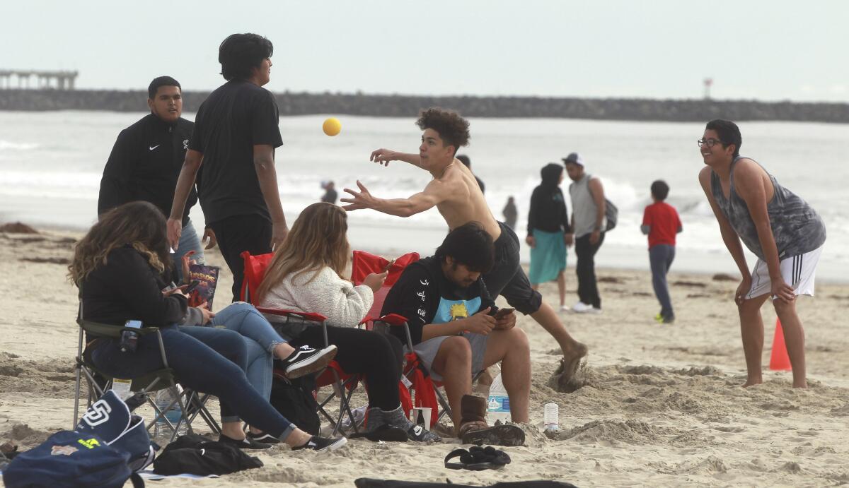 A group of young men play spike ball while friends sit nearby at Mission Beach on Friday.