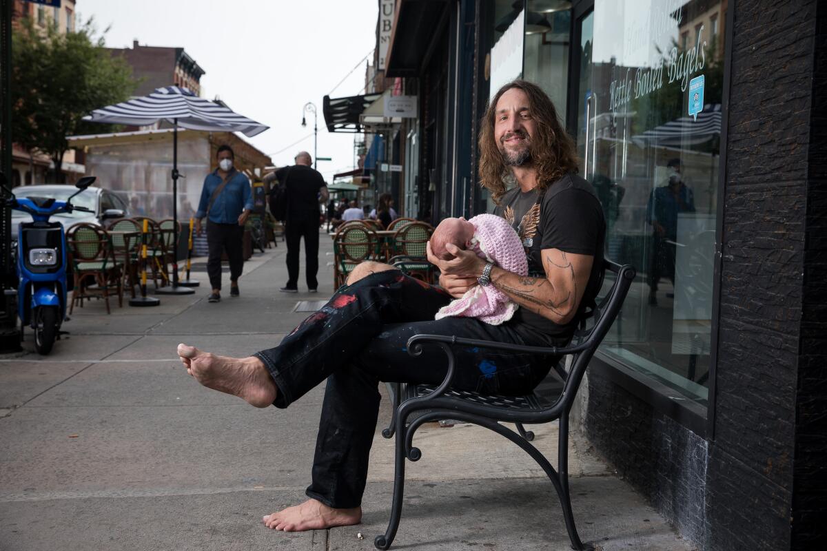 Joseph Arthur sits barefoot on a bench on a New York City sidewalk holding his 4 day-old daughter Alessia.