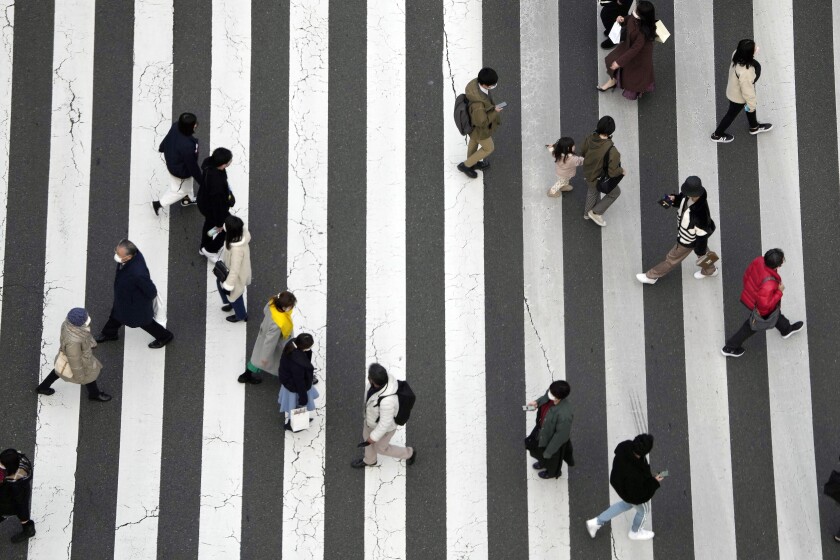 Varias personas, con mascarillas para ayudar a frenar la propagación del coronavirus, caminan por un paso de peatones en Tokio, el 17 de enero de 2022. (AP Foto/Eugene Hoshiko)