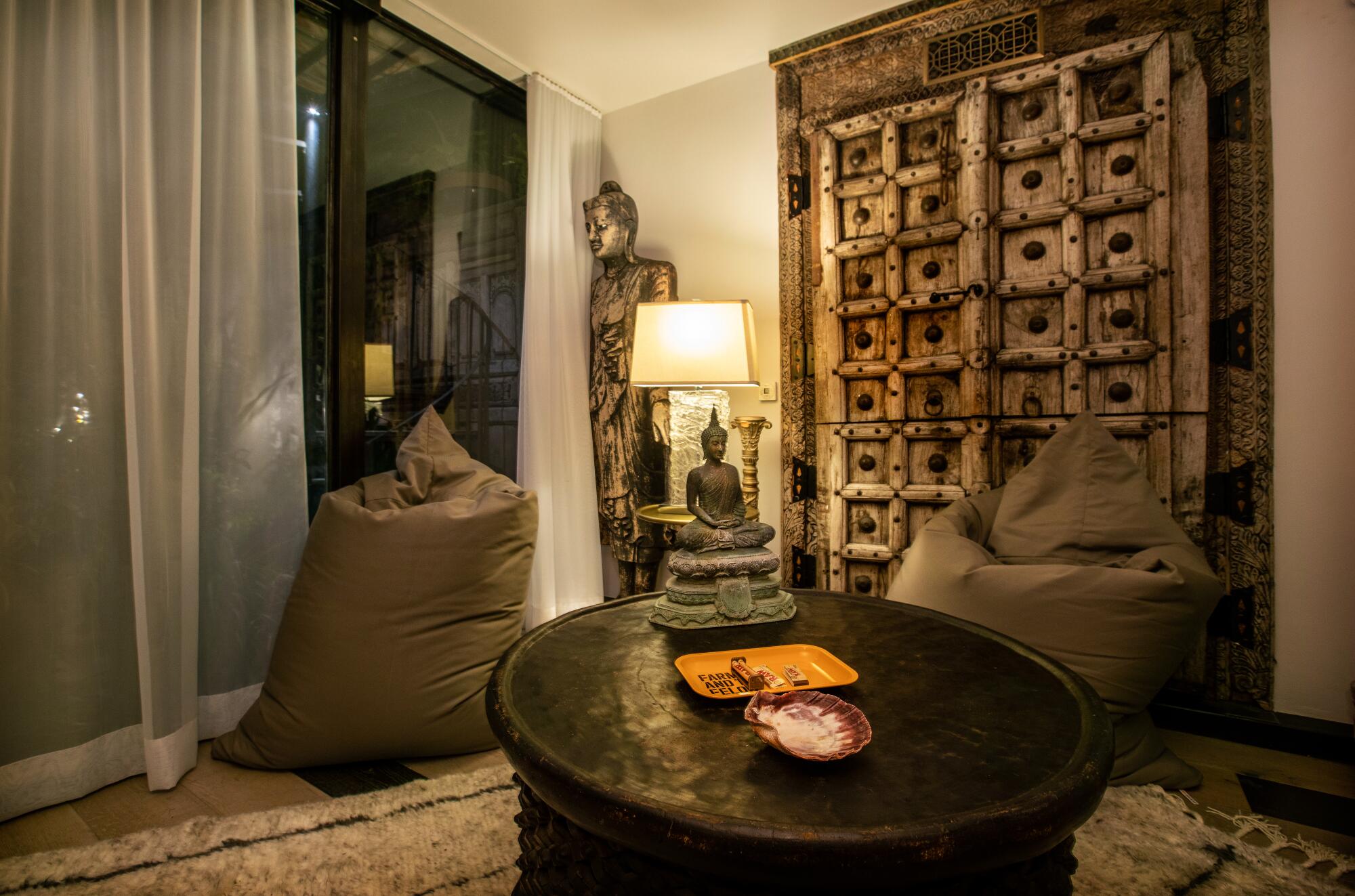 Two bean bag chairs, a Buddha statue and a large wooden door clustered around a coffee table in a cabana.