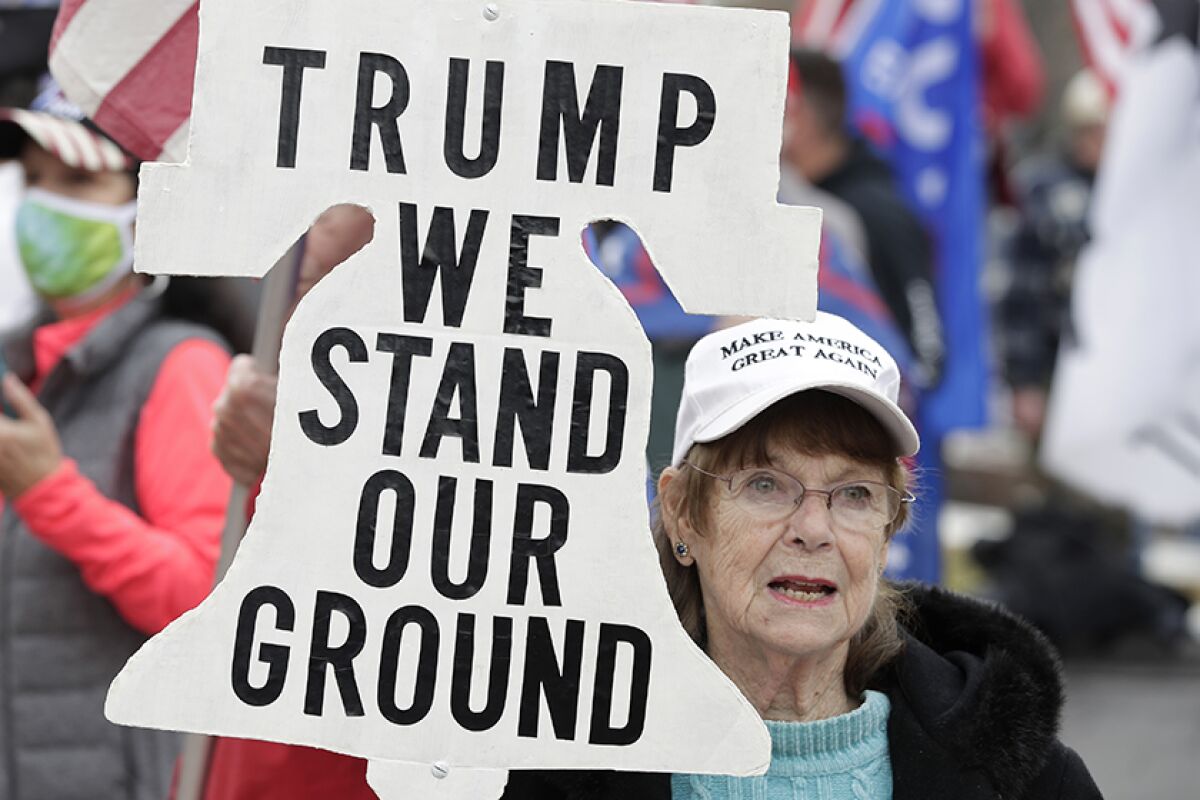 A Trump supporter attends a rally with a bell-shaped sign saying, "Trump we stand our ground."