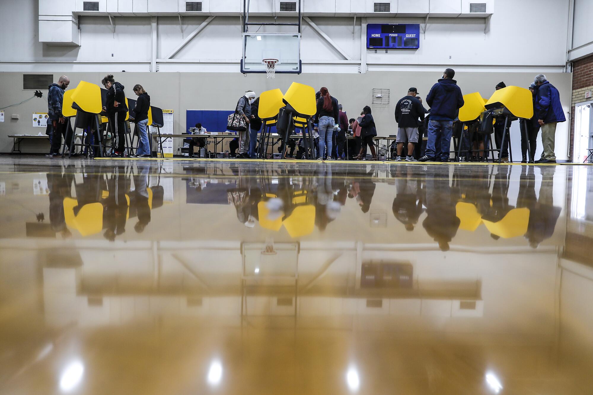 People stand at yellow voting booths in a basketball gym