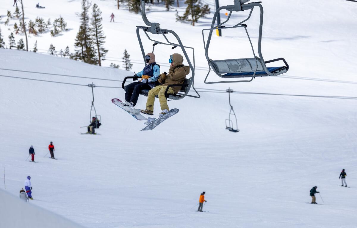 Skiers and snowboarders sitting on a ski lift, with people on the snow below.