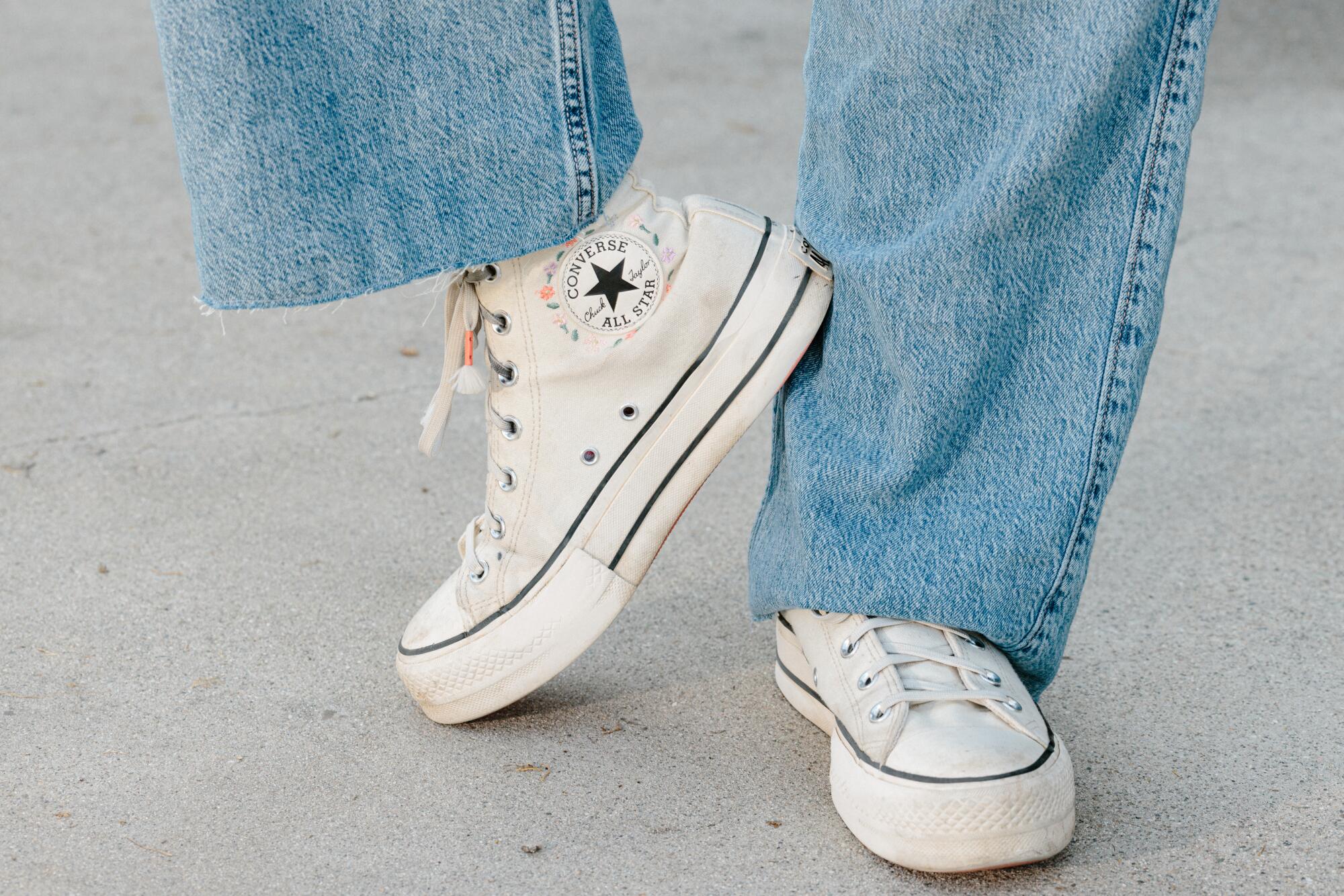 A detail of a person's white Converse shoes.