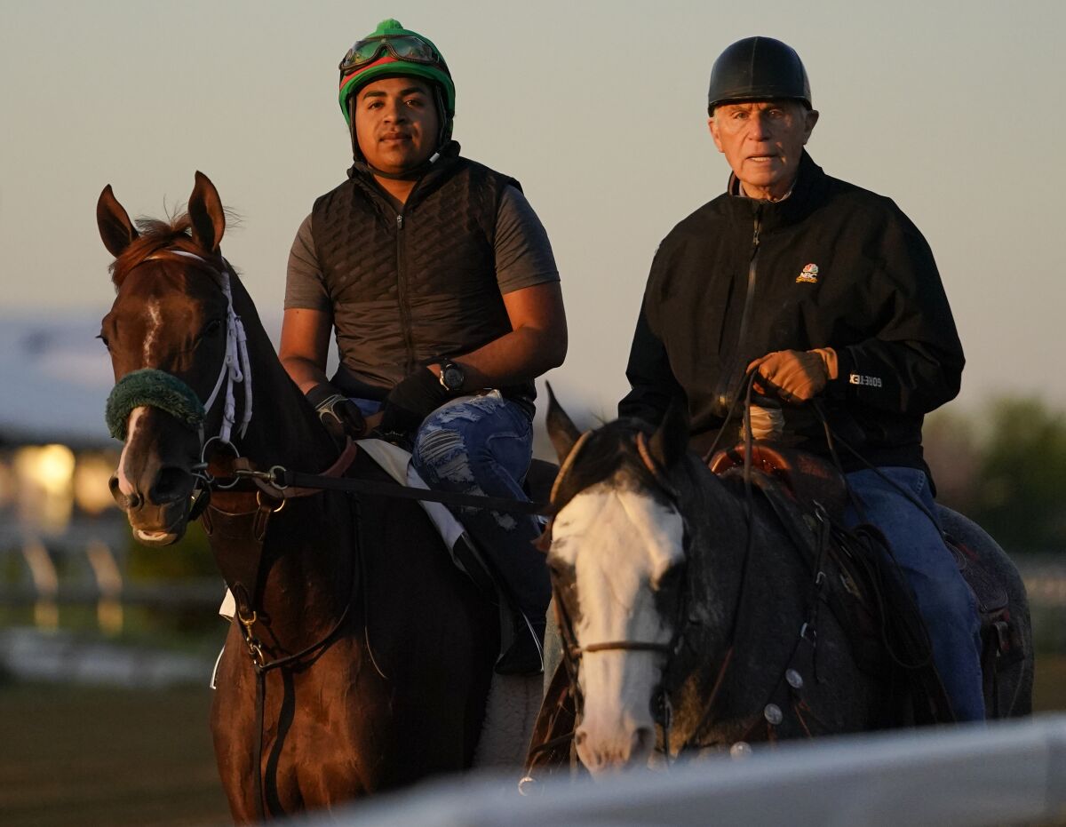 Horse trainer Wayne Lukas rides atop Riff as he helps exercise rider Oscar Quevedo and Preakness entrant Secret Oath.