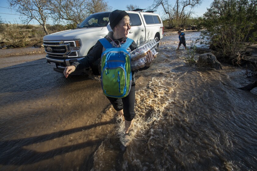 MALIBU, CA-DECEMBER 31, 2021: Brooke Dennis and her son Woody, 11, from Salt Lake City, Utah, make their way back to their flooded out campsite at Leo Carrillo State Campground in Malibu after spending the night at a Red Cross shelter set up at Malibu High School. Getting there first, ahead of them were her husband Matt and daughter Pepper. At least 50 people had to be rescued from the campground after significant rainfall sent a torrent of muddy water through the area, said Los Angeles County Fire Department spokesman Geovanni Sanchez. (Mel Melcon / Los Angeles Times)
