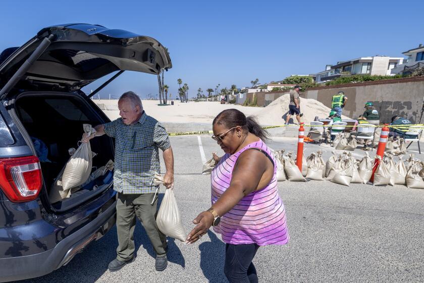 Seal Beach, CA - August 18: John Straub, left, a volunteer with West Orange County Community Emergency Response Team (CERT) loads sandbags for Cynthia Abernathy, of Lakewood, who plans to fortify her home ahead of anticipated high surf, strong winds and flooding from the approaching Hurricane Hilary in Seal Beach Friday, Aug. 18, 2023. As Hurricane Hilary continues its march toward Southern California, officials have issued an unprecedented tropical storm watch for the region. The watch is in effect for much of southwestern California, from the San Diego deserts to the San Bernardino County mountains and onto Catalina Island, something the National Hurricane Center said is a first for this area. A tropical storm watch indicates that tropical storm conditions are possible - meaning more than 39 mph sustained winds - within 48 hours, according to the hurricane center. (Allen J. Schaben / Los Angeles Times)