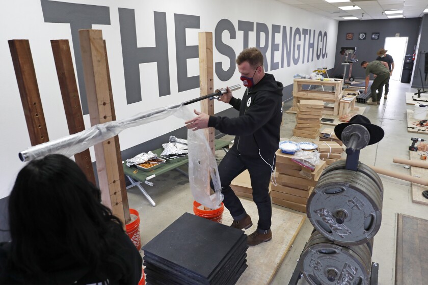 Owner Grant Broggi, center, sets up a wooden squat rack at the Strength Co. in Costa Mesa on Thursday.