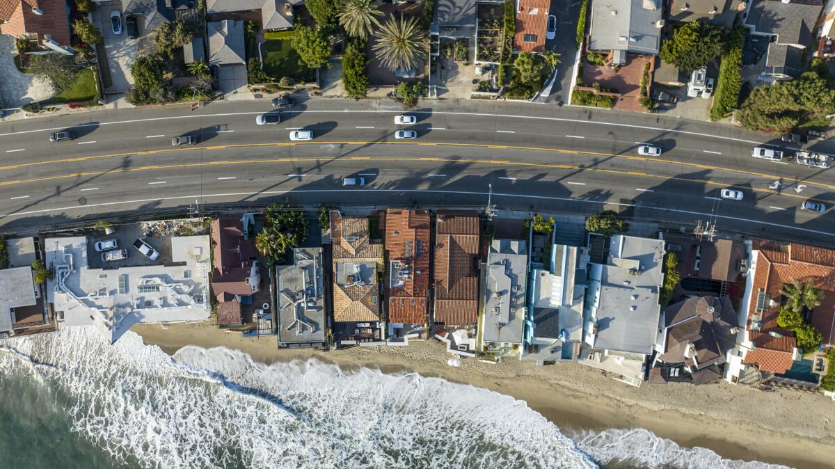 An overhead view of a road between rows of houses next to the ocean.
