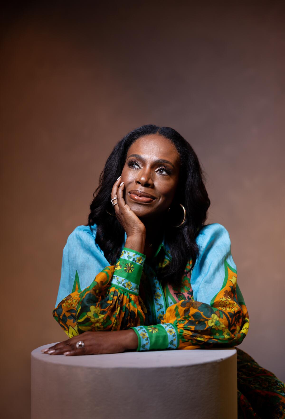 Sheryl Lee Ralph in a turquoise blouse with patterned sleeves and her chin resting on one hand