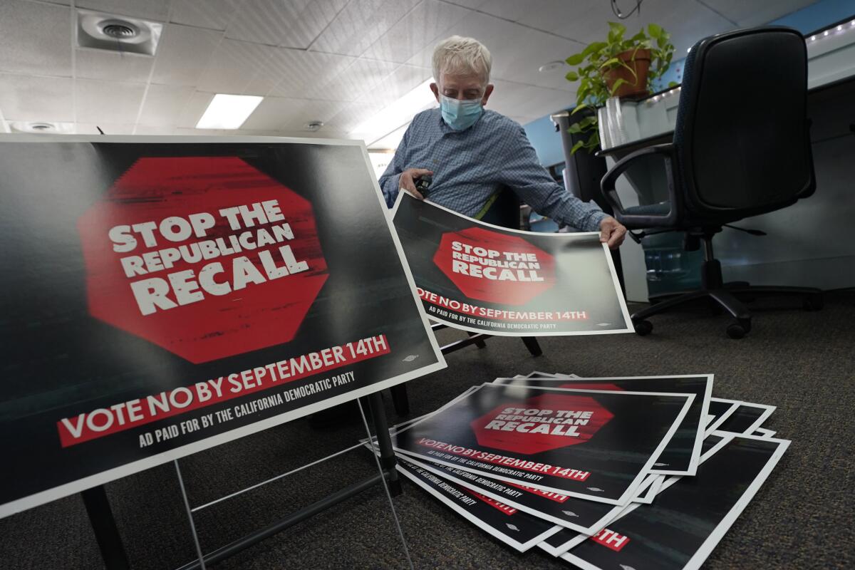 A man in a mask assembles signs that say "Stop the Republican recall"