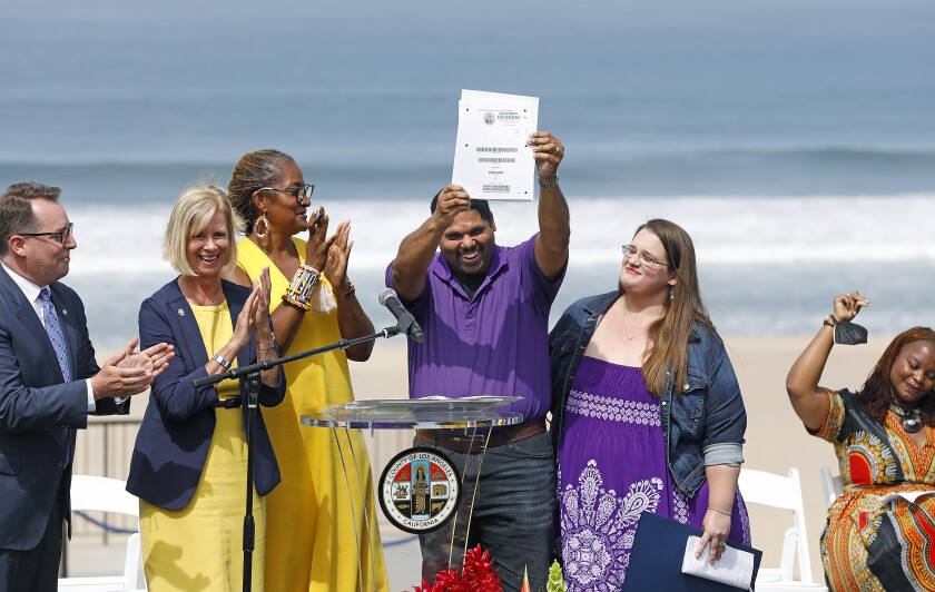 People stand behind a lectern as a man holds up a piece of paper. The beach and ocean are in the background.
