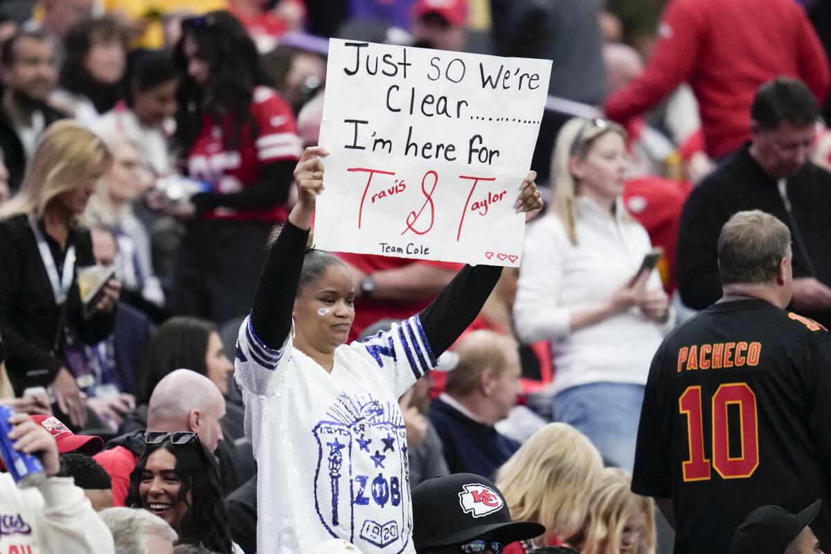 A fan holds a sign reading "I'm here for Travis and Taylor" at the Super Bowl.