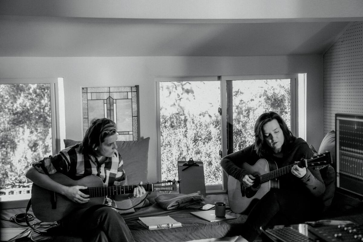 Two women play guitars in a room in a black-and-white photo