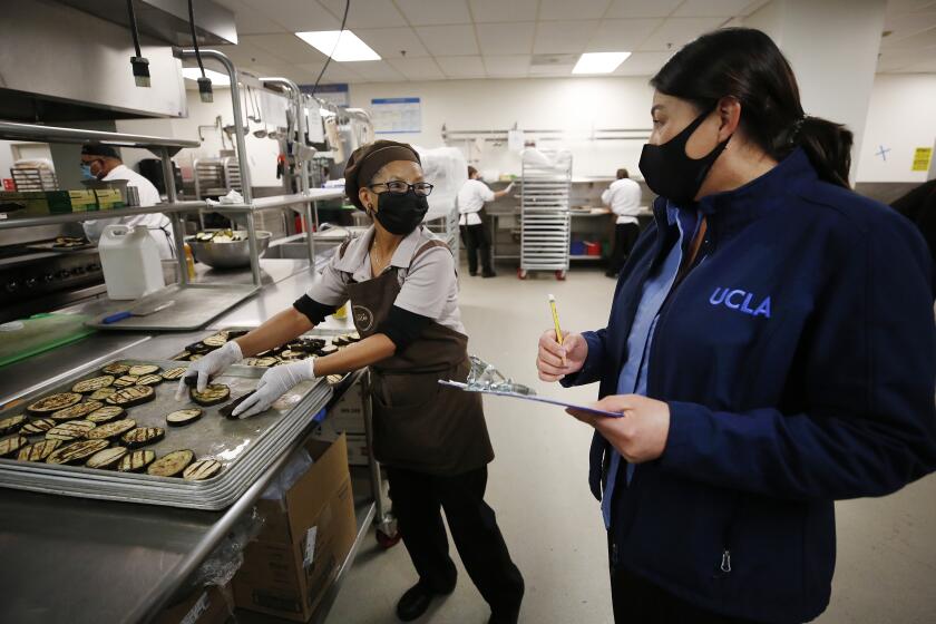 LOS ANGELES, CA - DECEMBER 02: UCLA Bruin Plate Residential Dining Restaurant General Manager Guadalupe Morales, right, reviews the checklist of items with Food Service Worker Norberta Gonzalez, left, preparing eggplant to be added to meals packaged for low-income families in partnership with the Venice Family Center. The financial impact of the pandemic on UC campuses is fueling calls among some chancellors for a tuition increase to address what they call the worst financial crisis of their careers. But at UCLA, Chancellor Gene Block has committed to no pandemic-driven layoffs through next June, as the campus is redeploying idled workers to areas of need. UCLA food service workers who no longer make hundreds of thousands of meals for on-campus students, are preparing food for low-income families. UCLA on Wednesday, Dec. 2, 2020 in Los Angeles, CA. (Al Seib / Los Angeles Times