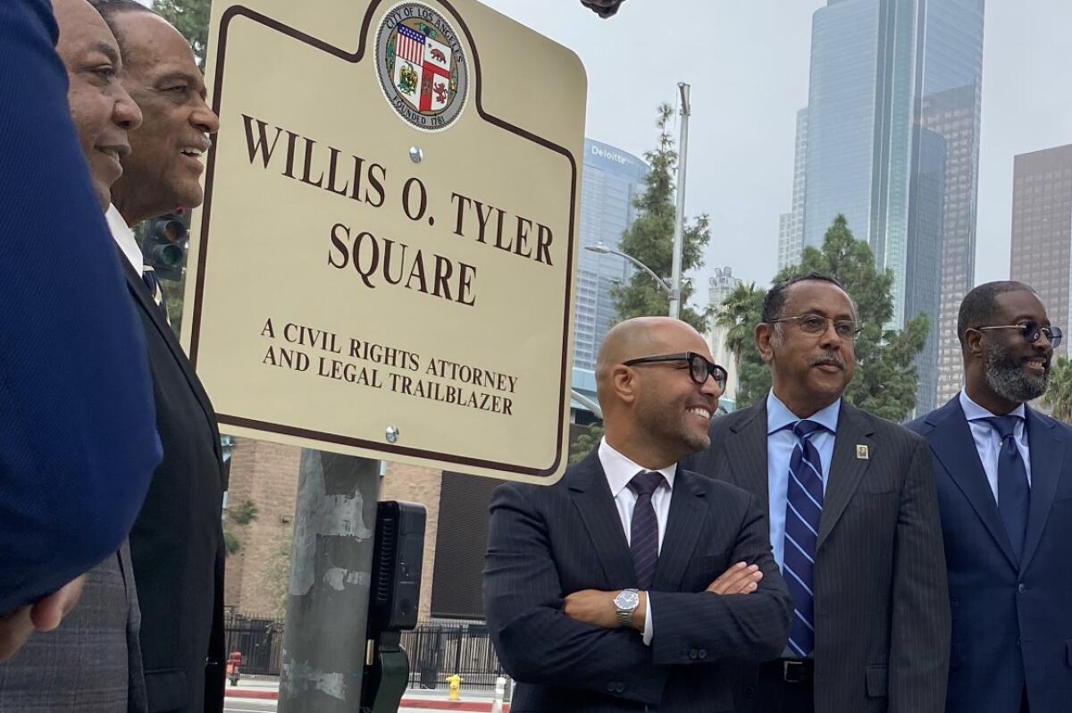 Three men in suits stand near a street sign 