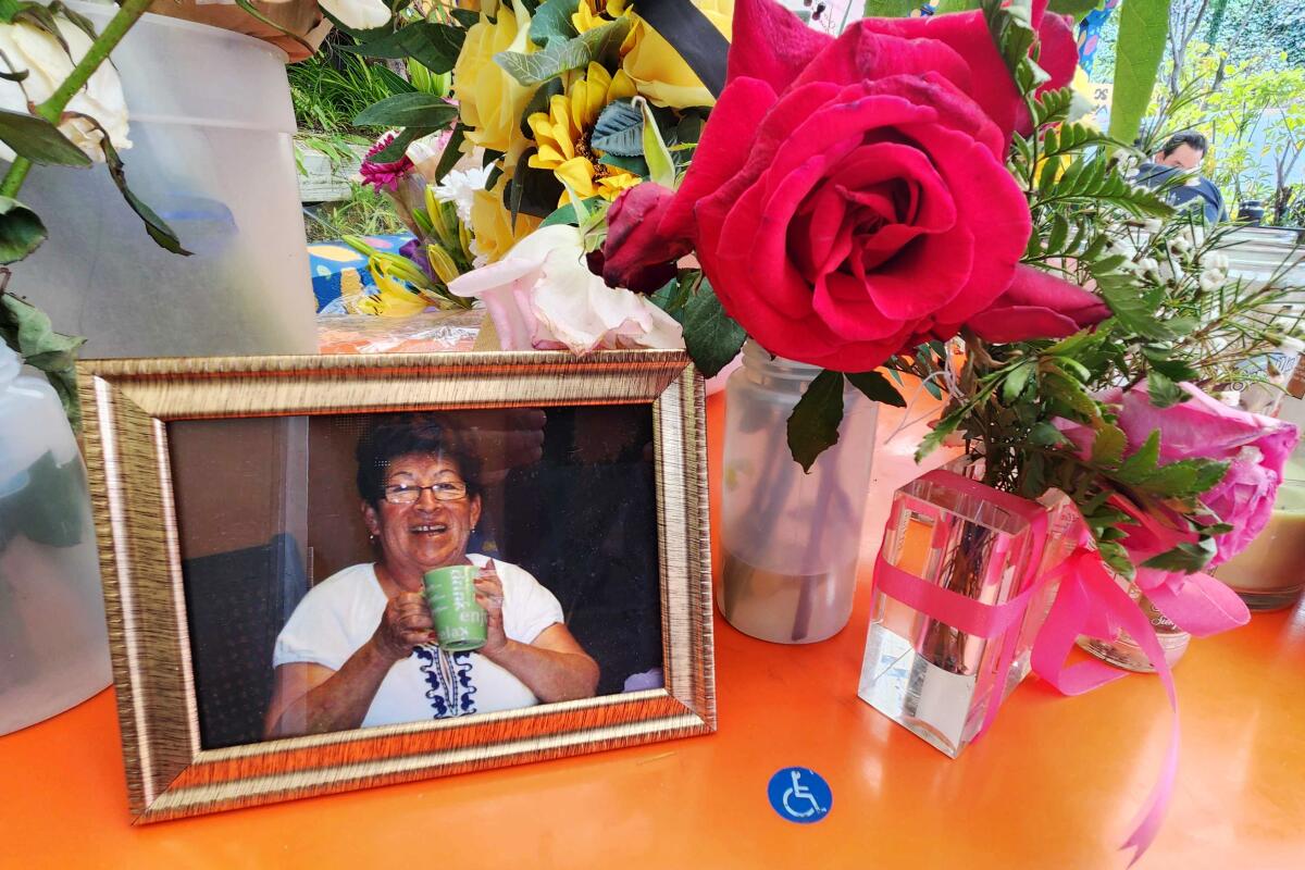 A flowers and candles memorial displays a framed image of a smiling woman holding a cup