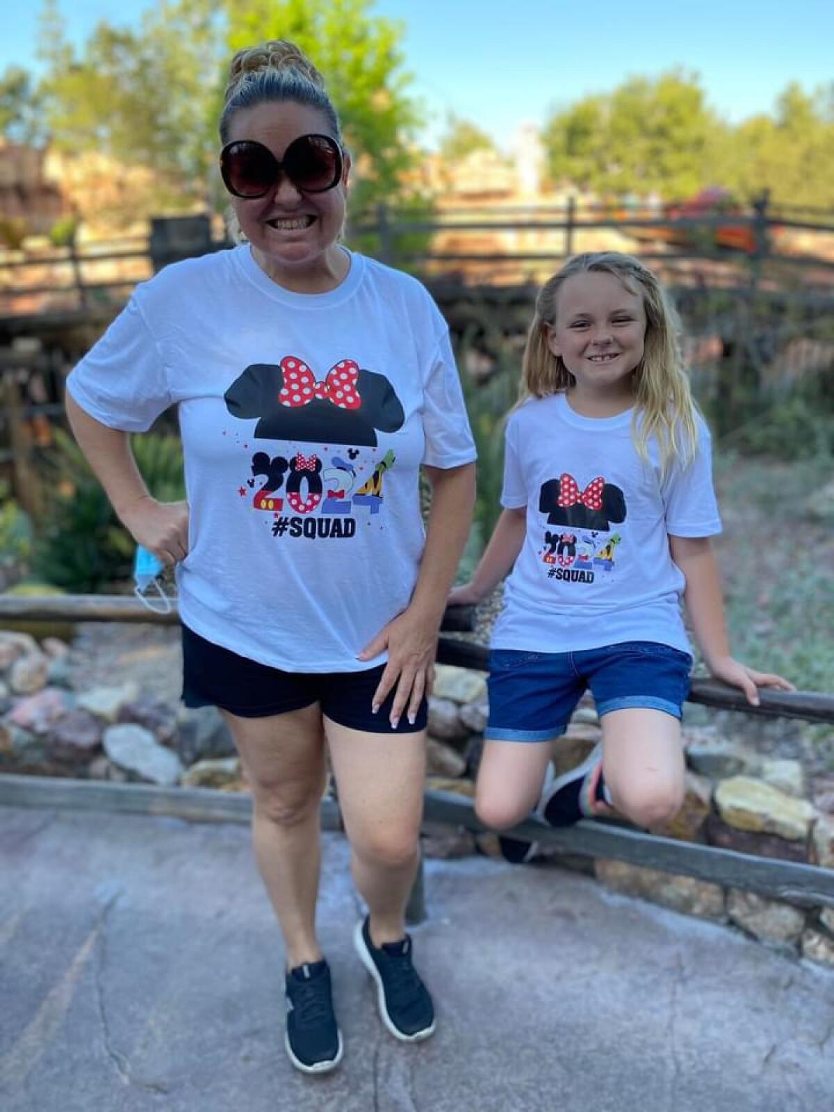 A woman and girl in matching Disney T-shirts pose for a photo.