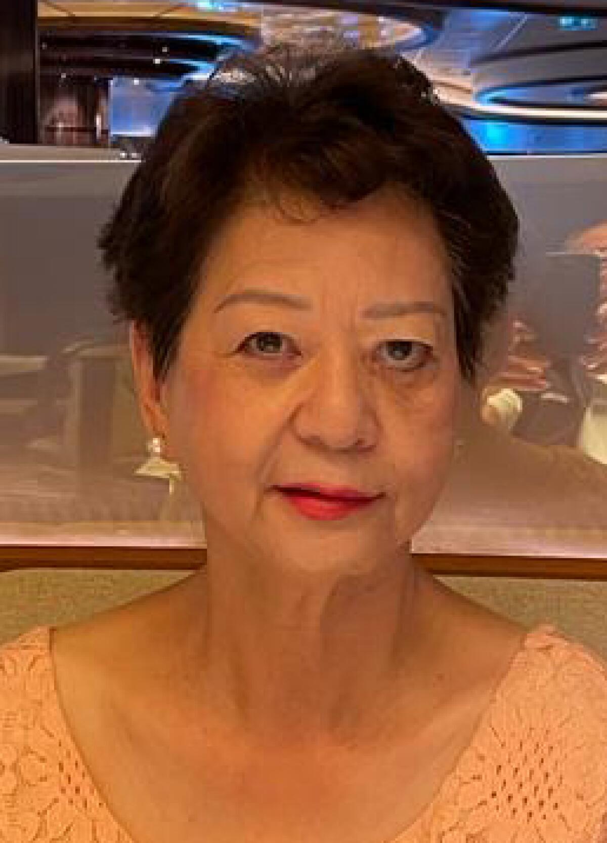 A woman with short brown hair wearing earrings, red lipstick and a peach-colored shirt