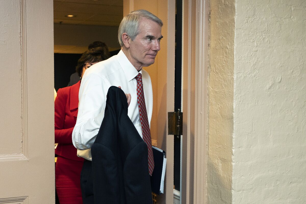 Rob Portman leaves a room carrying his jacket.