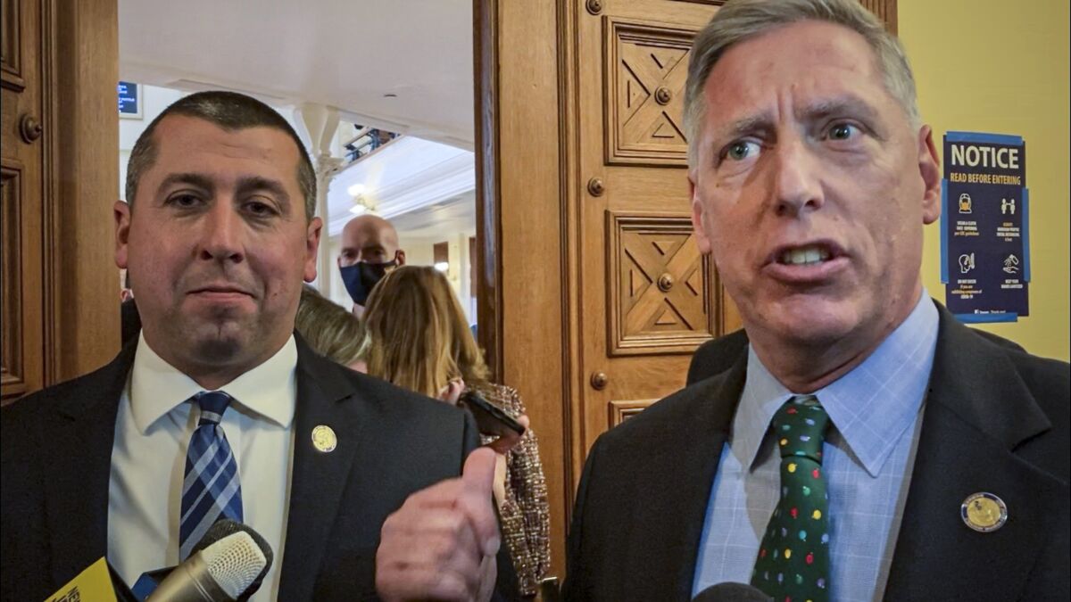 New Jersey Assembly member Brian Bergen, left, stands with fellow GOP Assembly member Erik Peterson, right, who speaks and gestures toward New Jersey State troopers blocking GOP lawmakers from entering the Assembly chamber because they did not show proof of a COVID-19 vaccination or a negative test, Thursday Dec. 2, 2021, in Trenton, N.J. The lawmakers decried the mandate, saying it was unconstitutional, though the troopers ultimately let the some of the legislators who declined to show their documents enter the chamber. It's unclear why. A message seeking an explanation was left with the state police. (AP Photo/Mike Catalini)