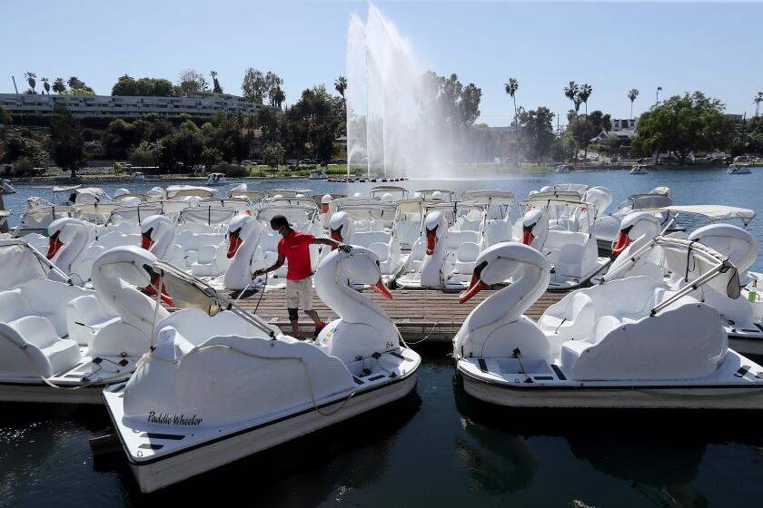 LOS ANGELES, CA - MAY 26:. A worker hoses off swan boats as Echo Park reopens to the public on Wednesday, May 26, 2021. The park was closed earlier this year after the eviction of about 200 homeless people who had taken up residence there. After its closure the park was cleaned and renovated. The evictions and closure remain a sore point for some local residents and homeless advocates. (Luis Sinco / Los Angeles Times)
