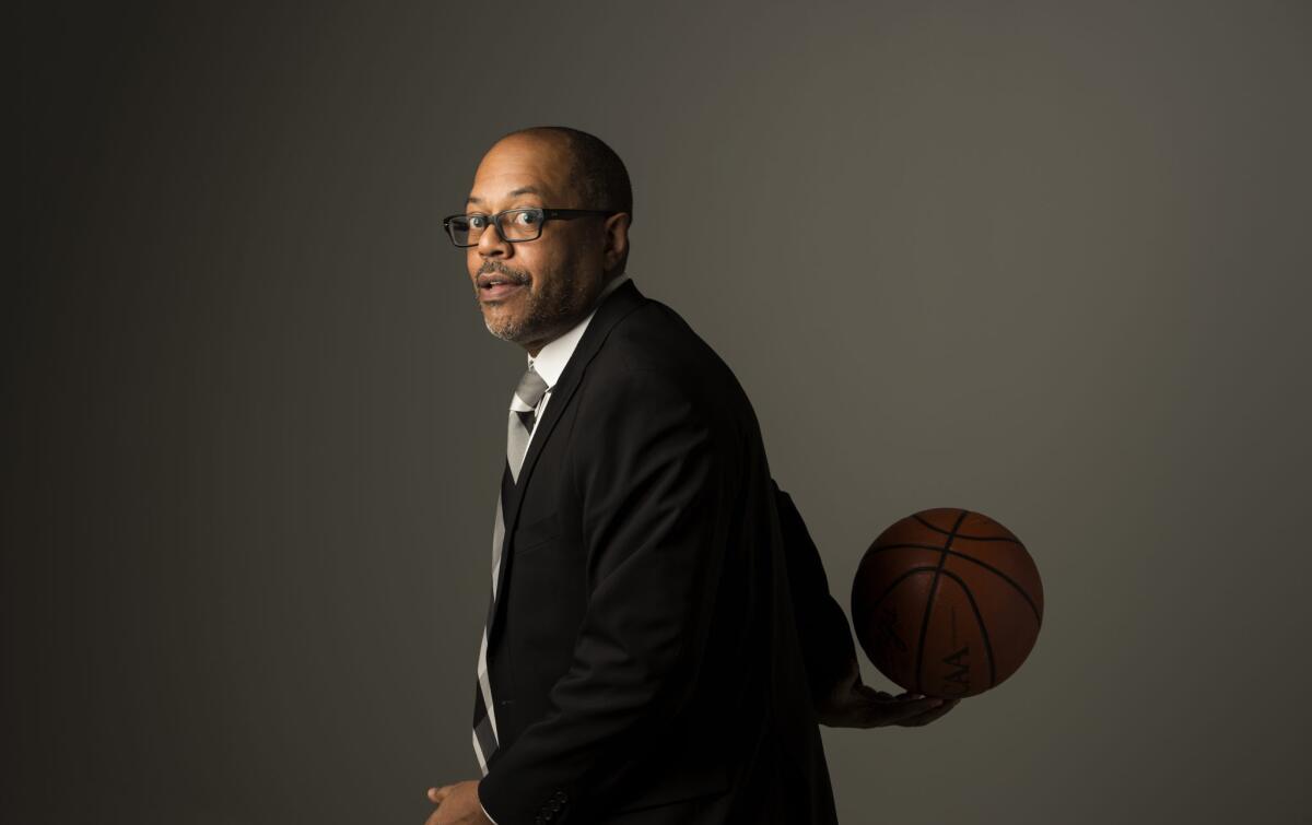 A man in a coat and tie holds a basketball behind his back.