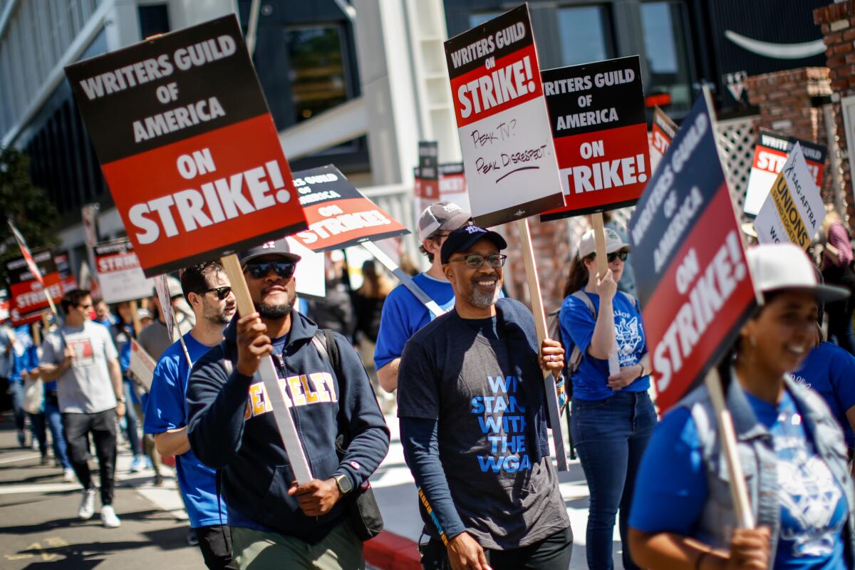 People picketing and carrying signs that read "Writers Guild of America on Strike"