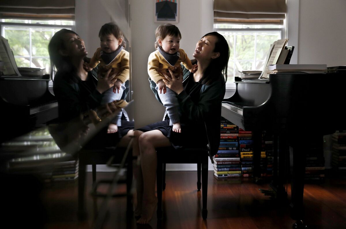 A woman holds a toddler while sitting at a piano bench