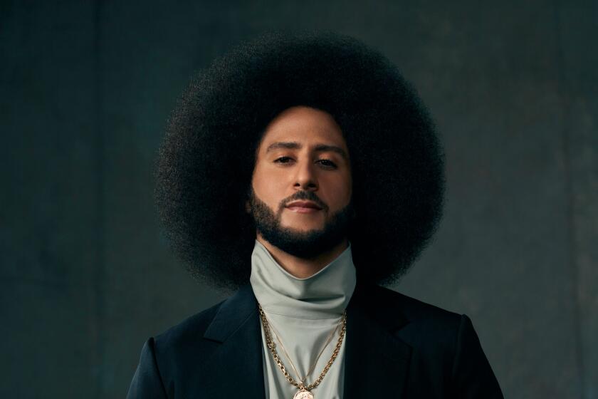 Colin Kaepernick in a dark jacket and gray turtleneck with his hands clasped in front of him