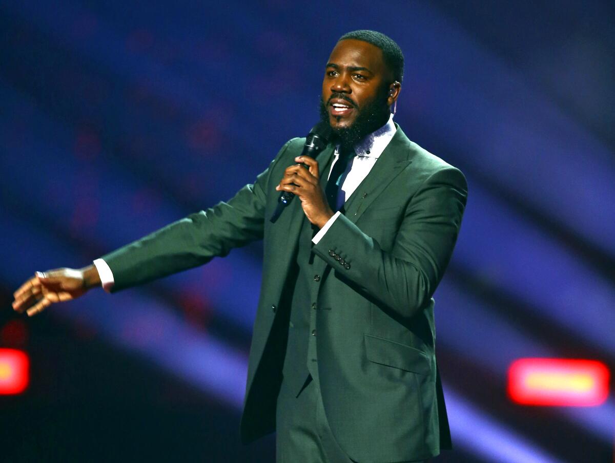 A man in a suit onstage speaks into a microphone.