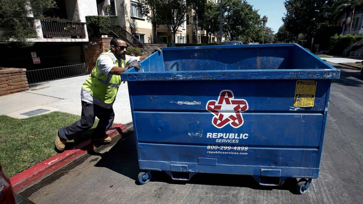 An employee with Athens Services, the trash hauler chosen by the city to serve the Westisde, moves a bin belonging to a 14-unit condominium building on Bentley Avenue in West Los Angeles.